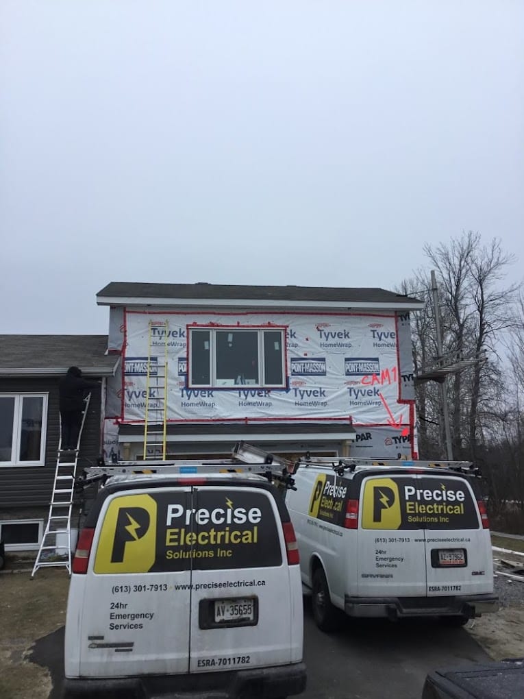 Electricians working on house exterior with electrical company vans.